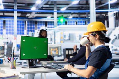 Güneş panelleri fabrika mühendisi kahve içiyor yeşil ekran bilgisayar kullanarak kalite kontrol yapıyor. Fotovoltaik fabrikası uzmanı içecek keyfi yapıyor. Robot kolları kalibre ediyor.