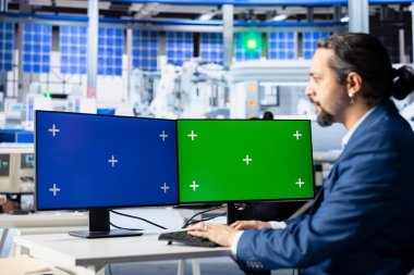 Fotovoltaik fabrikasındaki mühendis, izole ekran bilgisayar görüntülerindeki sistem kayıtlarını inceleyerek hataları tanımlıyor. PC monitörlerindeki üretim parametrelerini ayarlayan fotovoltaik fabrika işçisi