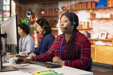 Ofisteki ekip çalışanı çağrı merkezi meslektaşları müşterilere soruları cevaplayarak yardım ediyor. Müşteri destek işyerindeki ajanlar müşterilerle konuşmak için kulaklık mikrofonunu kullanırlar.