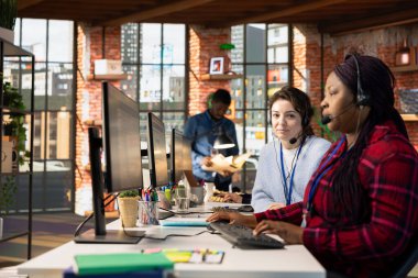 Müşteri hizmetleri çalışanının portresi PC 'deki şirket yazılımında iş arkadaşının izleme destek biletinin yanında. Ofis masasındaki çağrı merkezi çalışanı müşteri araması için destek bileti hazırlıyor.
