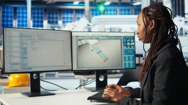 PC kullanarak fotovoltaik fabrikasındaki programcı robot kollarının güneş panellerini montaj hatlarına yerleştirdiği yazılımı güncelliyor. Bilgisayarda kodlama yapan kadın, güneş santrali makinelerini güncelleme, kamera A