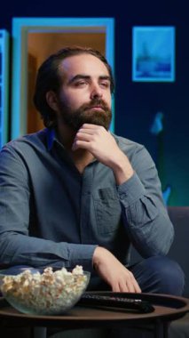 Televizyon ekranında gösterilen ilginç filmle kanepede oturan dikey video adam. Neon ışıklı oturma odasında canlı yayın yapan kişi, eğlenceli film sahnesinden büyülenmiş, dikkat çeken...