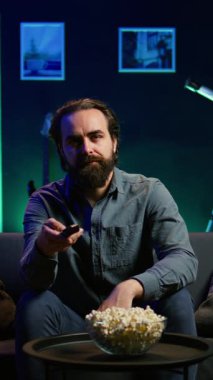 Dikey Videocu, evde kanepede dinleniyor. Evde televizyon izlerken ağzına patlamış mısır tıkıyor. Abur cubur yiyen ve neon ışıklı oturma odasında TV şovları yapan kişi, kamera B
