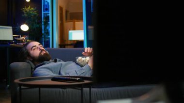 Neşeli ev sahibi kanepeye uzanıyor, TV 'de film izliyor, komik sahnelerle eğleniyor. Ev sinemasında eğlenen, iyi filmler izleyen, patlamış mısır yiyen, kamera B