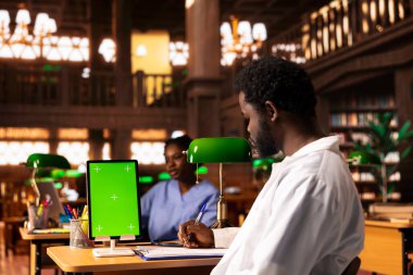 Siyahi tıp öğrencisi kütüphanede krom anahtar ekranın yanındaki dava dosyalarını inceleyerek, tıbbi uygulamalar üzerine bir derse ya da çalışma oturumuna hazırlanıyor. Tıp fakültesi öğrencisi kariyer için öğreniyor..