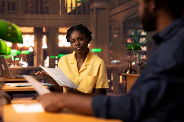 Afrika kökenli Amerikan takımı sınıf notlarını karşılaştırıyor ve kütüphanede araştırma yapıyor. Sınav hazırlıkları için akademik veritabanına danışıyor. Eğitim amaçlı takım çalışması yapan iki öğrenci.