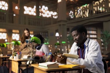 Klinikteki tıp kitapları veritabanına danışmak için kütüphanedeki muayenehanesinde çalışan Afrikalı bir doktor. Stajyerlik yapan genç bir öğrenci sağlık sektöründe kariyer yapmayı öğreniyor..