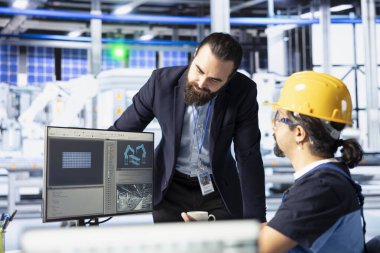 Fotovoltaik fabrikası iş arkadaşları beyin fırtınası yapıyor, maksimum verimlilik için sistem ayarları yapıyor. Konuşan mühendisler, güneş panelleri üzerinde birlikte çalışarak montaj hatlarını yapılandırıyorlar.