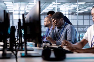 Sunucu çiftliğini veri işleme gereksinimleri için optimize ederken yorgun mühendis baş ağrısı hissediyor. Stresli adam veri merkezi dişlilerinin verimli çalışmasını sağlamak için fazla mesai yapıyor.