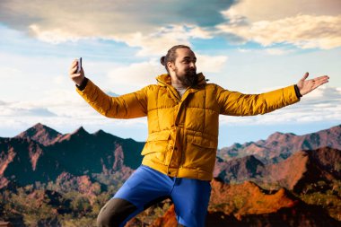 Erkek içerik yaratıcısı bulutlardaki dağ zirveleriyle çevrili bir video kaydediyor, bir dağ tepesine tırmanıyor ve sosyal medya izleyicileri için canlı yayın yapıyor. Maceracı ruh..