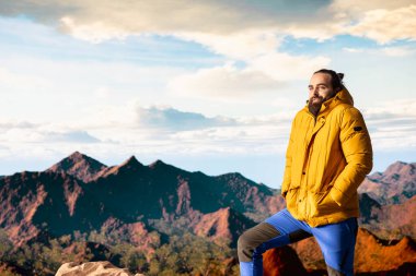 Gezgin, yüksek bir dağ sırasının kenarında tek başına duruyor, bulutlara ve çarpıcı panoramik manzaraya bakıyor. Memnun yürüyüşçü kişisel gelişim ve azim gösteriyor.