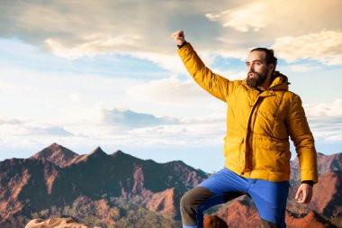 Gururlu kaşif, engebeli tepeler ve dramatik bulutlarla çevrili yüksek rakımlı bir dağın zirvesinde kutlama yapıyor. Zafer pozu başarılı bir tırmanışın ve sağlığın heyecanını yakalar..
