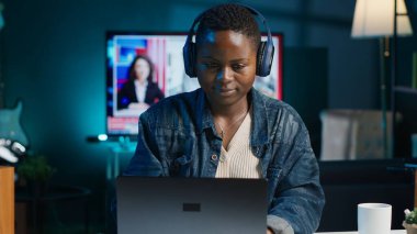 Freelancer müzik dinlerken takım projesi için kişisel ev ofisinde bilgisayar görevleri yapıyor. Uzaktan çalışan, gece geç saatlere kadar çalışan, dizüstü bilgisayarda yazan, kulaklık takan, kamera A