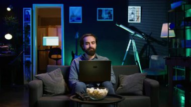Adam dizüstü bilgisayarda klavyede, neon ışıklı dairede oturuyor, koltukta oturuyor ve patlamış mısır kasesiyle televizyon seyrediyor. Not defterindeki görevleri arka planda film oynatarak çözen telesekreter, kamera B