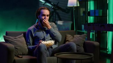TV 'de film izlerken ve patlamış mısır yerken evde yemek yiyen bir adam. Yemek yerken boğazı tıkanan, koltukta heimlich manevrası yapan, hayatı için savaşan, kamera A