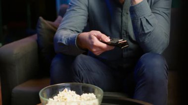 Kanepede oturup uzaktan kumandayla filmlere göz atmak için yaklaş. Ev sahibi tarafından TV ve kamera A 'da kanal değiştirmede kullanılan uzaktan kumandaya odaklan