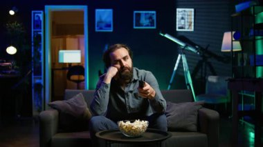 Sıkıcı adam evde kanepede dinleniyor, TV 'de film seyrederken patlamış mısır yiyor. Tembel insan abur cubur yiyor ve RGB 'deki TV kanallarından geçiyor oturma odası, kamera B