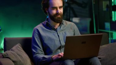 Neon ışıklı dairede dizüstü bilgisayar kullanarak TV 'de şok edici bir son dakika haberi izleyen adam. Televizyonun sesini açan kişi, dizüstü bilgisayar ve kamera A 'yı kullanarak koltukta otururken yaşanan olaylara şaşırdı.