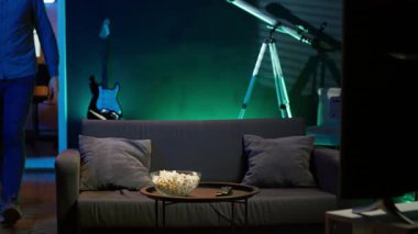 Adam eve geliyor, kanepede dinleniyor, TV 'de gösterilen filmleri izlerken patlamış mısır yiyor. Apartmana giren, abur cubur yiyen ve neon ışıklı oturma odasında yayın yapan kişi, kamera A