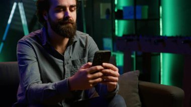 Adam gece geç saatlerde evinde kanepede oturmuş RGB 'deki akıllı telefondan arkadaşlarına mesaj atıyor. Arkadaşlarıyla sohbet etmek için cep telefonu kullanan kişi, rahat neon ışıklı bir apartman dairesinde, kamera A.