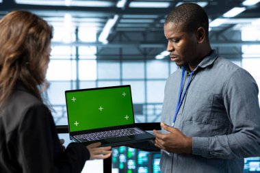 Sunucu çiftliğinde çalışan mühendislerden oluşan bir ekip verileri analiz etmek için yeşil ekran dizüstü bilgisayar kullanıyor. Veri merkezindeki altyapıyı inceleyen çalışanlar, sistem bütünlüğü ve güvenliğinin sağlanması için model defter kullanıyorlar.