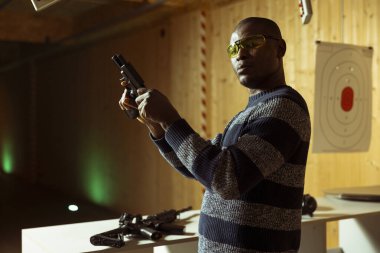 Koruma gözlüğü takan, silah dolduran, hedef vurmaya hazırlanan poligon müşterisinin portresi. Atış poligonundaki adam silah dolduruyor, koruyucu ekipman takıyor.