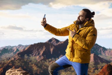 Azimli maceraperest panoramik dağ manzarasından zevk alır. Doğanın ve yükselen zirvelerin nefes kesici bir manzara yarattığı tepenin muhteşem arka planıyla selfie çeker..