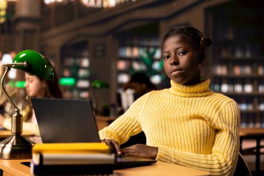 Öğrenci kız İnternet üzerinden bilgi okuyor ve kütüphanede notlar alıyor, teorik çalışmalara odaklanıyor ve akademik bir ortamda sınıf ödevlerini tamamlıyor. Eğitim çalışmaları.