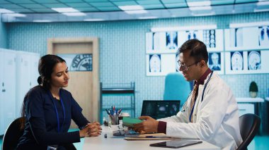 Hintli bir adam, reçeteye antibiyotik ve ilave ilaçlar yazıyor. İlaç için doz öneriyor ve profesyonel talimatlar veriyor. Doktor hasta için tavsiye veriyor. Kamera B.