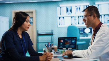 Kabinede tıbbi test sonuçlarını tartışmak için hastalarla yapılan doktor toplantısı, röntgen taramalarını yorumlamak için gelişmiş teşhis araçları kullanmak, profesyonel bir sağlık yaklaşımı sergilemek. Kamera B.