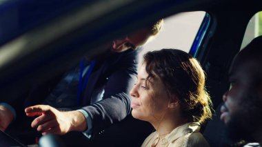 Showroom satıcısı test sürüşünü bitirdikten sonra müşterilerine tablet üzerinde satın alınabilir ekstra araba özellikleri gösteriyor. Satış temsilcisi araç kataloğu gösteriyor. Karı kocaya ait. Kamera A 'da.