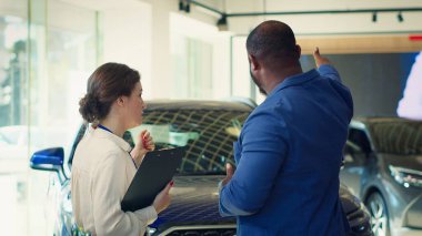 Kondisyon değerlendirmesi ve bilgi sağlandıktan sonra müşteriye kontörlü araç satan kadın, kullanılmış arabanın güvenilirliği ve bakımıyla ilgili müşteri kaygılarını ele alıyor, kamera A