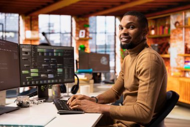 Başlangıç ofisinde bilgisayar kullanarak makine öğrenmesini sağlayan algoritmalar tasarlamak ve uygulamak için gülümseyen bilişim uzmanının portresi. Afro-amerikan teknoloji işçisi hata düzeltme için kod incelemesi yapıyor.