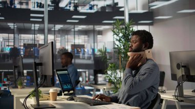 Boyun yaralanmasından muzdarip siyah genel müdür rahim boynu köpüğü giyer ve masasında rahatsız edici bir pozisyonda mücadele eder. Analizci günlük işlerini çözmeye çalışıyor ama acı çekiyor. Kamera B.