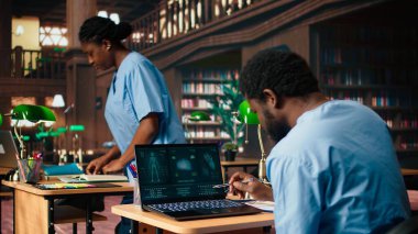 Tıp fakültesi öğrencisi anatomi araştırma kağıtlarından kişisel notlar alıyor, tıp kariyeri için sağlık yöntemleri okuyor. Kampüs veritabanındaki kitapları kullanan bir erkek öğrenci. Kamera A.