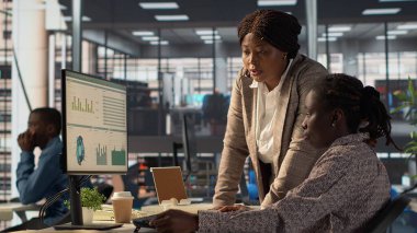 Kadın çalışan ve yönetici bir çalışma istasyonunun etrafında toplanarak idari görevleri daha hızlı çözmek için hedefler ve stratejik çözümler üzerinde tartıştılar. İş hedeflerini ve kilometre taşlarını hizalamak. Kamera A.