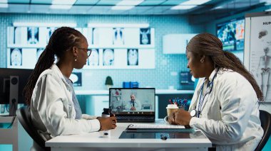 Doktor, bir hastayla video konferansı için uzman doktoru arıyor. İkinci bir görüş için tele sağlık danışmanlığı yapıyor. Klinikte yüksek teknolojili ekipman kullanan tıbbi personel. Kamera B.