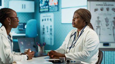 Afrika kökenli Amerikalı bir hasta tıbbi bir muayenehanede bir doktorla görüşüyor, kişisel bakım veya tedavi için teşhis raporlarını ve analizleri tartışıyor. Sağlık için tavsiyede bulunuyorum. Kamera A.