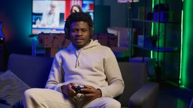 Evdeki kanepede oturan genç adam oyun konsolunda video oyunları oynayarak rahatlıyor, neon ışıklı apartman dairesinde internetteki çoklu oyuncu ve spor turnuvasında rekabet ederek gevşiyor. Kamera A.