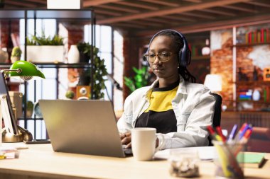 Evde müzik dinleyen, internette gezinen, ödev yapan, internette bilgi araştıran bir öğrenci. Evde kulaklık takan bir kadın okul işleri için dizüstü bilgisayarda makaleler okuyor.