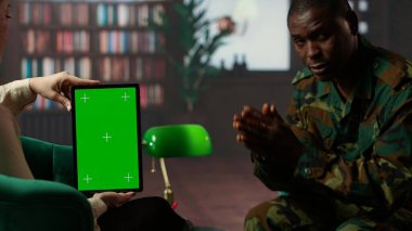 Siyahi asker terapi seansında kroma anahtar ekranının yanında ağlıyor. Travma sonrası stres bozukluğu ve travma sonrası iyileşme için profesyonel destek arıyor. Silahlı kuvvetler ruhsal sağlık hizmetleri ile ilgili tartışmalar. Kamera B.