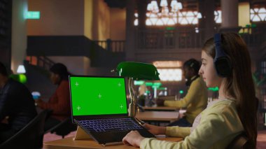 Ergen öğrenci kütüphanede ödev oturumunda izole bir şekilde bilgisayar üzerine dijital bir makale yazıyor. Ders hazırlıklarının altını çiziyor. Dizüstü bilgisayarı üzerinde çalışan odaklanmış bir kız. Kamera A.