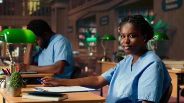 Afrikalı Amerikalı tıp fakültesi öğrencisi bir kütüphanede farmakoloji notları okuyor, sınavlara hazırlanıyor ve sağlık kariyerlerinde ilerliyorlar. Önlüklü kız tıp fakültesinin başarısı için çok çalışıyor. Kamera B.