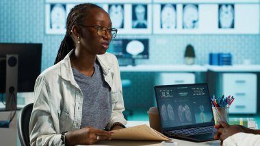 Afro-Amerikalı doktor ve hasta tıbbi kayıtlar hakkında derin bir konuşma yapıyorlar, sonuçları açıklıyorlar ve bir tedavi planı hazırlıyorlar. Sağlık ve iyileşme için ilaç. Kamera A.