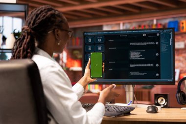 Mutlu kadın yeşil ekranlı telefon kullanıyor, AI Chatbot cevap yazarken bilgisayarın önünde video görüşmesi yapıyor. Neşeli Afro-Amerikan vatandaşı, Mockup smartphone 'daki video konferansı sırasında LLM programını kullanıyor