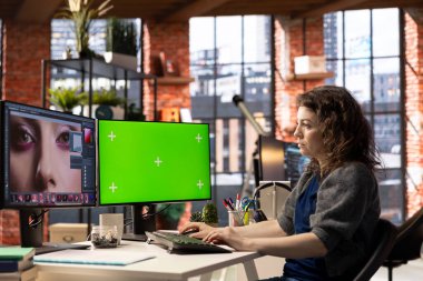 Kadın grafik tasarımcısı iyi organize edilmiş bir çalışma alanında fotoğraf rötuşlaması için düzenleme yazılımı ve yeşil ekran kullanır. Genç editör, yaratıcı bir sanat kariyeri için gerekli dijital araçları kullanıyor.