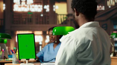 Genç tıp öğrencisi kroma anahtarının yanındaki sınavlar için araştırma yapıyor, yeşil bir lamba altında farmakoloji belgelerini gözden geçiriyor. Sınav hazırlıklarına ve tıp kariyerlerine odaklanıyorlar. Kamera B.