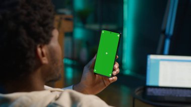 Afrikalı Amerikalı uzaktan kumandalı işçi, modern şık oturma odasındaki kanepede oturarak evinin rahatlığıyla çalışmak için cihazın üzerinde kroma anahtar ekranını kullanıyor. İnternetteki mutlu genç adam. Kamera A.