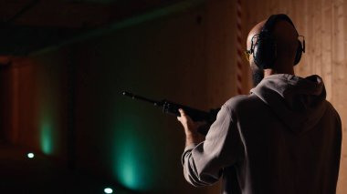 Atış poligonunda tüfekle ateş eden, işitmeyi engellemek için kulaklık takan bir adam. Yarı otomatik silahlı şahıs eğitimi, silah seslerinden zarar görmemek için güvenlik teçhizatı kullanımı, kamera A