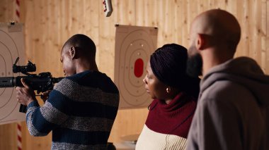 Atış poligonu güvenlik görevlisi, kurallara uymalarını sağlamak için yarı otomatik silahı müşterilere güvenli bir şekilde nasıl doldurulacağını gösteriyor. Atış poligonu çalışanı düzgün saldırı tüfeği kullanmayı öğretiyor, kamera B